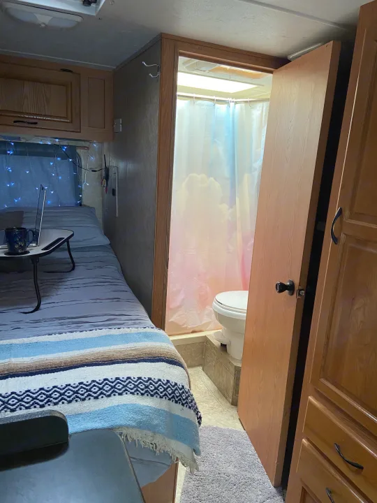 Cozy RV rental interior: a compact bedroom with blue lights and laptop, and an adjacent bathroom with a cloud shower curtain.. Thor Motor Coach Four Winds Majestic 2009