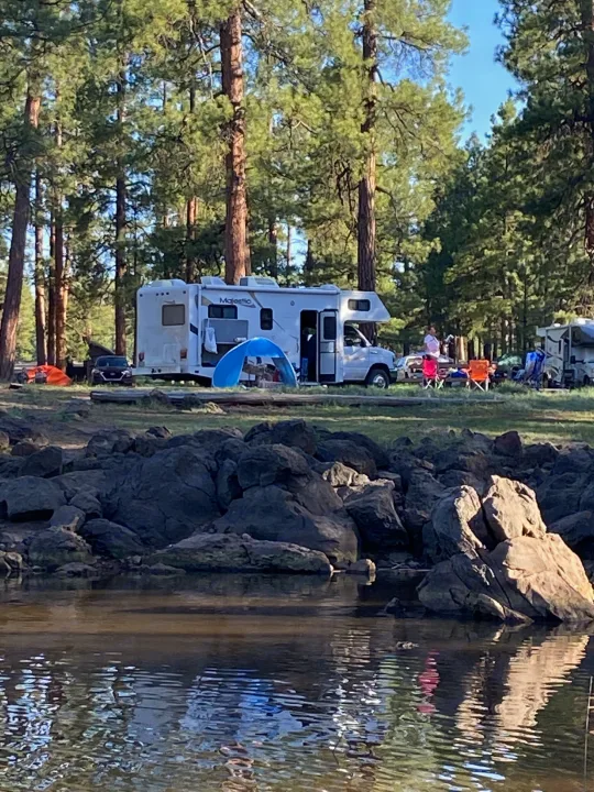 An RV rental at a lakeside campsite, surrounded by pine trees, where people are enjoying a peaceful outdoor retreat.. Thor Motor Coach Four Winds Majestic 2009