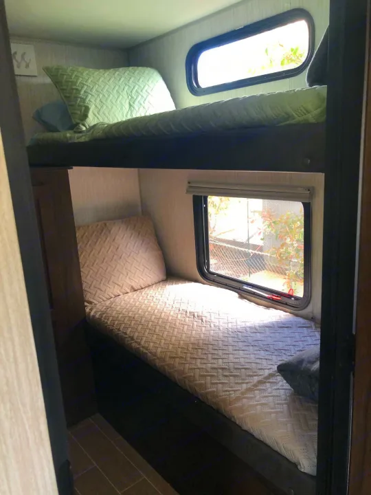 RV rental bunk beds offer comfy sleeping. Top bunk has green bedding & window, bottom has light bedding & window.. Forest River Grey Wolf 29te 2021