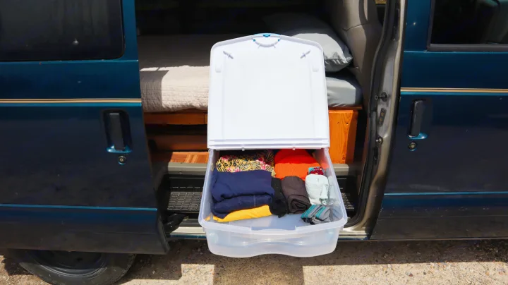 Smart **RV rental** storage: A clear bin of folded clothes slides out from a blue van, perfect for organized mobile living.. Chevrolet Other 2003