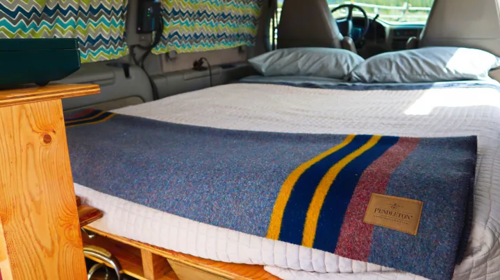 Cozy RV rental interior shows a made-up bed with a colorful Pendleton blanket, ready for comfortable travels.. Chevrolet Other 2003