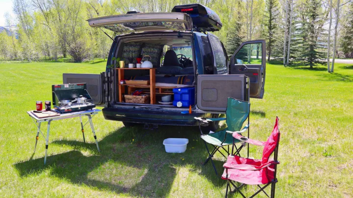 Van life setup for an RV rental adventure. Campervan with outdoor kitchen, chairs, and bed in a scenic field.. Chevrolet Other 2003