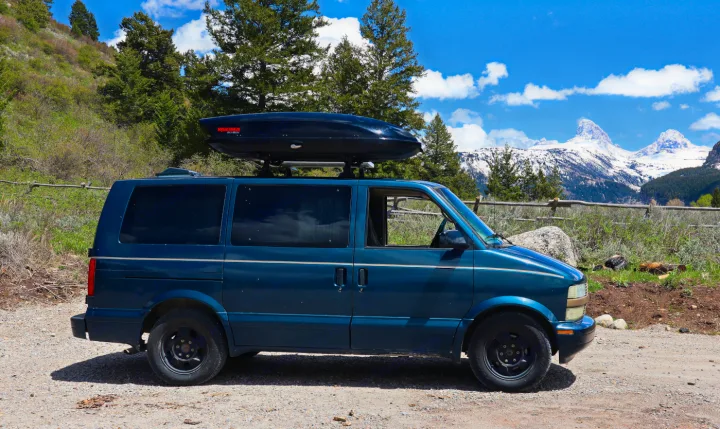 Blue van with Yakima cargo box, parked by snow-capped Grand Teton. Perfect for your next RV rental adventure!. Chevrolet Other 2003