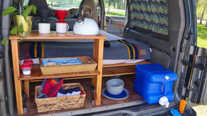 RV rental: Well-equipped camper van interior featuring kitchen shelves with kettle, coffee gear, storage, and cozy bed.. Chevrolet Other 2003