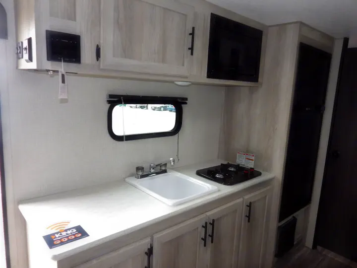 This rv rental features a compact kitchen with a sink, two-burner stovetop, microwave, and refrigerator, all within a light-wood interior.. KZ 181BH 2021
