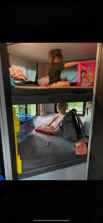Kids enjoying their RV rental bunk beds. An older girl on top, a toddler playing with toys below, amidst travel comforts.. Work and Play Work and Play Trailer 2020