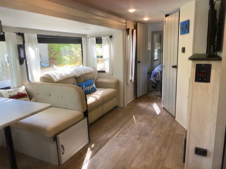 Spacious RV rental interior with a cozy dining booth, comfy sofa, and wood-look flooring, ideal for travel.. Forest River Vibe 2021