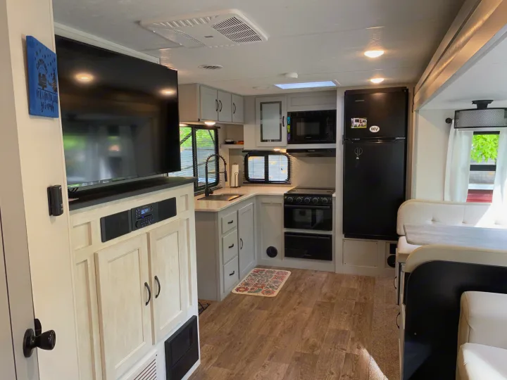 Bright RV rental interior with a modern kitchen, built-in entertainment center, and dining area for comfortable travel.. Forest River Vibe 2021