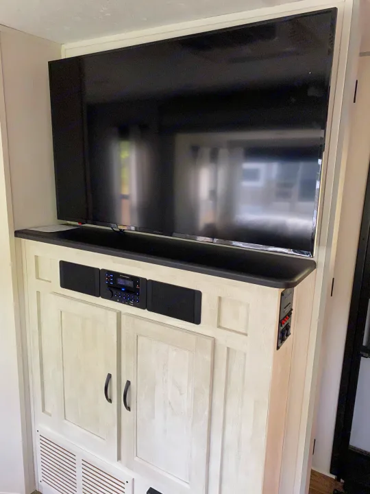 RV rental features: A large TV, integrated stereo, speakers, and control panel within light wood cabinetry. Your onboard entertainment hub.. Forest River Vibe 2021