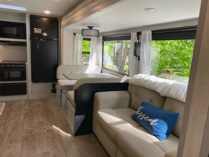 Modern RV rental interior featuring a well-equipped kitchen, comfortable dinette, and inviting sofa with green views outside.. Forest River Vibe 2021