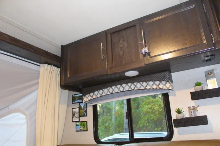 Cozy RV rental interior with dark wood cabinets, a window showing trees, and decorative items like framed photos.. Dutchmen Kodiak 2019