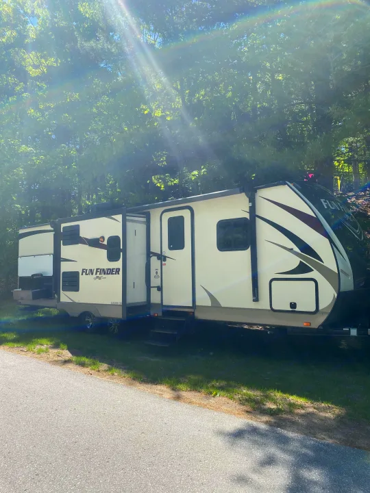 A sun-drenched Fun Finder RV rental, a cream-colored travel trailer, parked at a lush forest campsite.. Other Fun Finder 2017