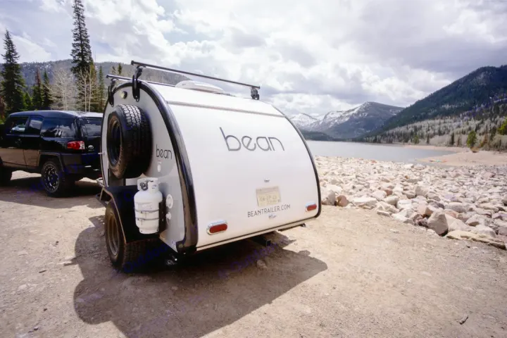 Bean teardrop rv rental parked by a scenic mountain lake, ready for adventure & camping with an SUV.. Bean Trailer Mean Bean 2021
