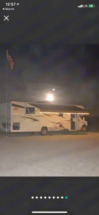 Nighttime rv rental under full moon. RV with string lights, deployed awning, American flag visible.. Winnebago Minnie Winnie 2015