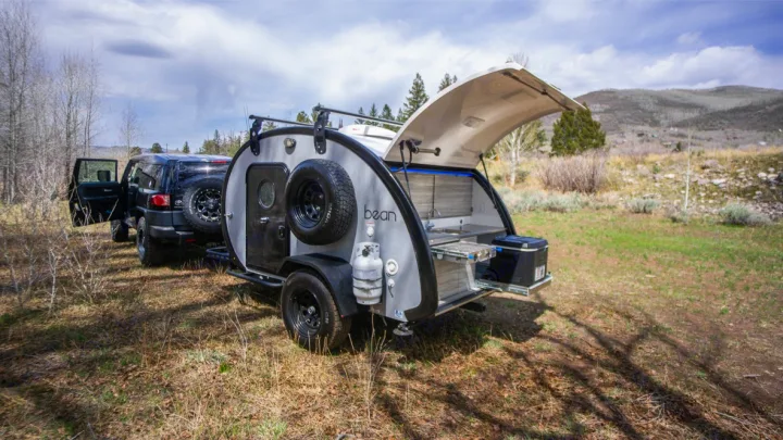 A black Toyota FJ Cruiser tows a teardrop RV rental camper with an open outdoor kitchen, perfect for off-grid adventures.. Bean Trailer Mean Bean 2021