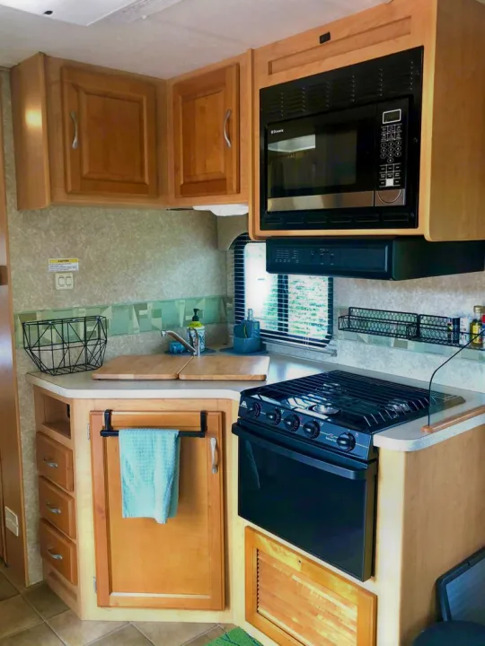 This RV rental kitchen features wood cabinets, black microwave, stove, and sink for convenient cooking on the go.. Thor Motor Coach Four Winds Five Thousand 2007