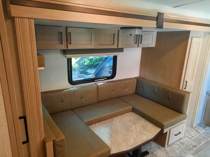Explore this modern RV rental's U-shaped dinette, featuring light wood cabinets, tan cushions, and a functional table.. Forest River Rockwood Mini Lite 2021