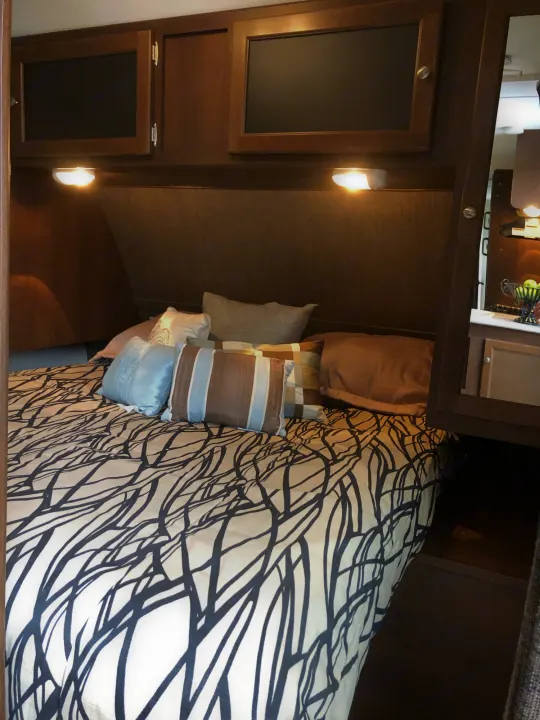 RV rental bedroom showcasing a patterned bed, wood cabinets, and integrated lighting.. Keystone Bullet 2015