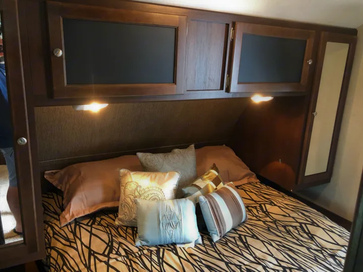 RV rental bedroom with a neatly made bed, decorative pillows, and built-in wooden cabinets above. Reading lights illuminate the space.. Keystone Bullet 2015