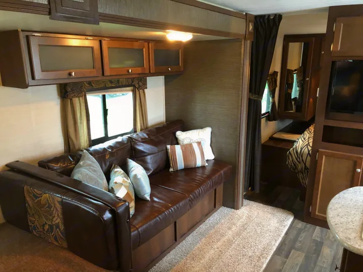 Spacious RV rental living area featuring a comfy brown sofa, overhead cabinets, and warm lighting.. Keystone Bullet 2015
