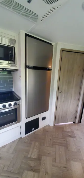 Modern **RV rental** kitchen with stainless steel microwave, stove, & refrigerator on herringbone floors.. Palomino Puma 2021