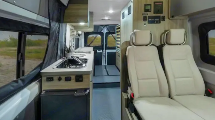 Modern RV rental interior featuring a kitchenette with sink, stove, and fridge, plus comfortable light-colored passenger seats.. Winnebago Solis 59PX 2022