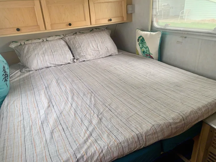 Comfortable RV rental bed featuring striped sheets, decorative pillow, and wood cabinets. Window view of yard.. T@B T16 2008