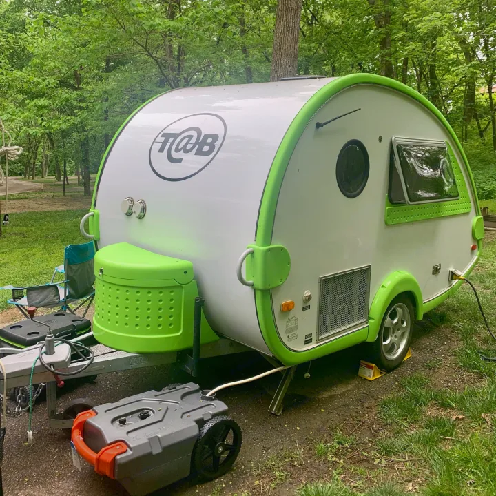 This T@B teardrop rv rental is set up at a wooded campsite, showing its lime green trim & portable waste tank.. T@B T16 2008