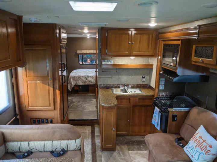 Spacious RV rental interior featuring a bright kitchen, comfortable living area, and a glimpse of the rear bedroom.. Coachmen Leprechaun 2018