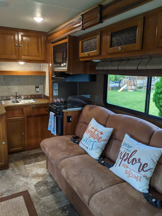Cozy rv rental interior featuring a kitchen, comfortable couch with pillows, and a scenic window view.. Coachmen Leprechaun 2018