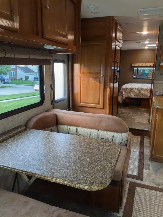 Spacious RV rental interior featuring a dinette, large window with outdoor view, and a peek into the bedroom area.. Coachmen Leprechaun 2018