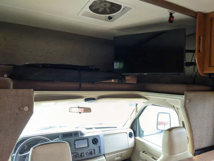 View inside an RV rental: driver's cockpit, over-cab bunk with TV, ceiling fan & textured walls. Perfect for travel!. Coachmen Leprechaun 2018