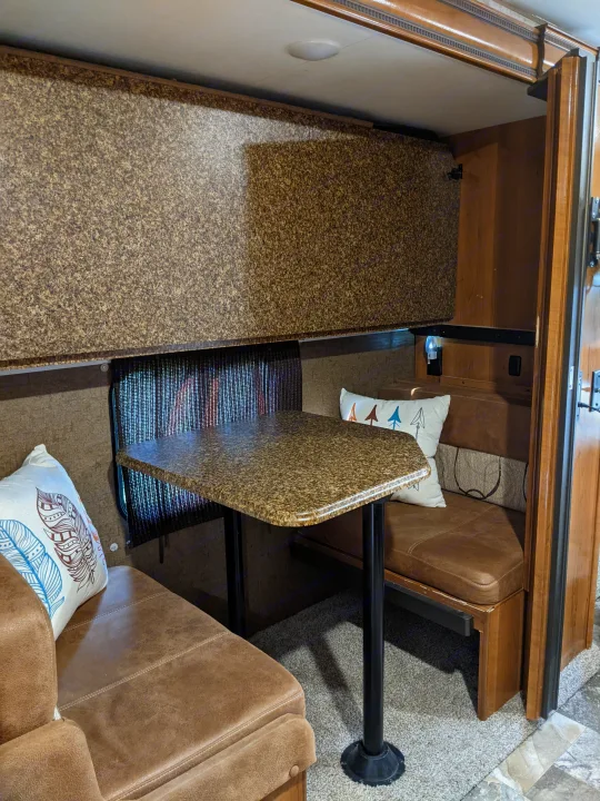 Enjoy this RV rental's cozy dinette: brown benches, granite-look table, and a clever overhead bunk.. Coachmen Leprechaun 2018
