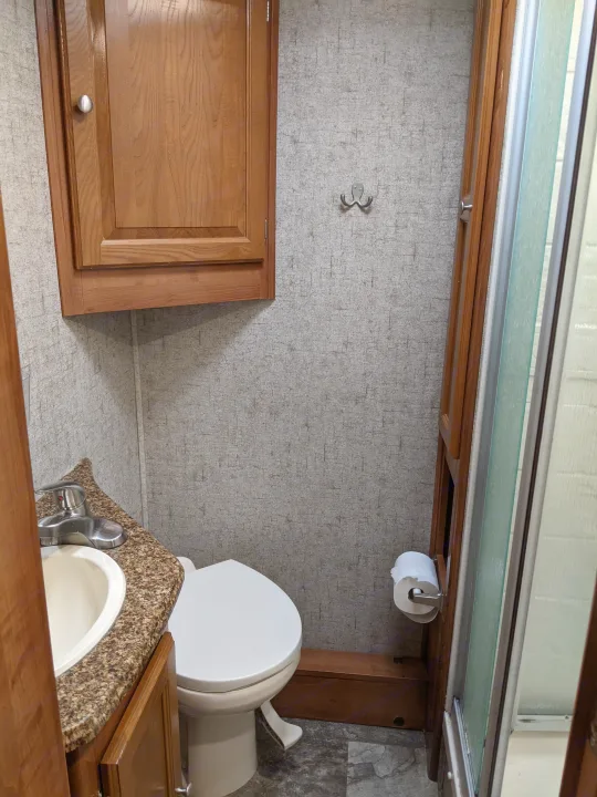 Compact RV rental bathroom with sink, toilet, overhead cabinet, and shower, providing essential amenities in a small space.. Coachmen Leprechaun 2018