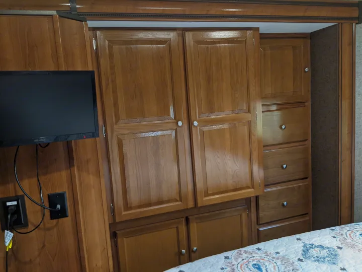 Detailed view of an RV rental bedroom showing wood cabinets, pull-out drawers, and a mounted TV for compact living.. Coachmen Leprechaun 2018