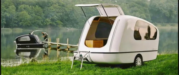 Modern rv rental trailer parked on grass by a lake, with a person on a pier beside a matching boat. Serene outdoor leisure.. Sealander Sealander 2021