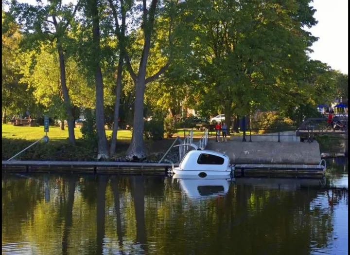 This unique, white 'RV rental'-like boat is docked at a park, reflecting on calm water. Perfect for aquatic adventures.. Sealander Sealander 2021