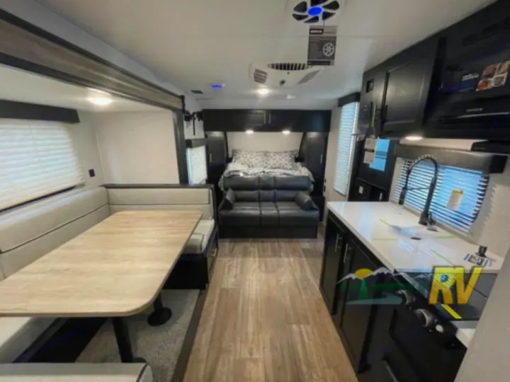 Spacious rv rental interior featuring a light wood floor, dinette, dark kitchen, and bed with sofa.. Forest River Cherokee Wolf Pup 16PFBL 2021