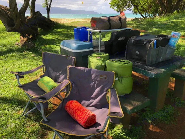 RV rental ready for beachside camping. Gear includes chairs, cooler, sleeping bags, and picnic items by the Maui ocean.. Ford Econoline 2009
