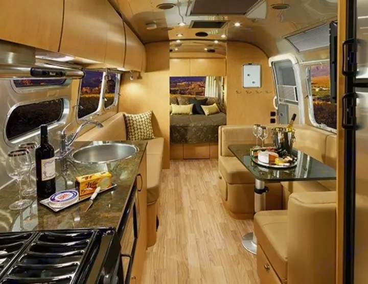 Spacious RV rental interior. Features a modern kitchen, dining booth with treats, and a private bedroom for travel comfort.. Airstream Flying Cloud 2016