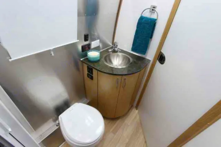 Compact rv rental bathroom, featuring a toilet, corner sink vanity with storage, and modern metallic finishes.. Airstream Flying Cloud 2016
