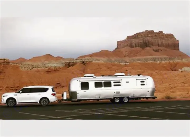 White SUV towing an Airstream travel trailer (RV rental) against a stunning desert backdrop. Ideal for road trip adventures.. Airstream Flying Cloud 2016