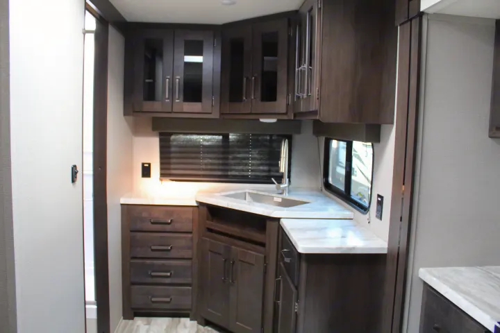 Modern RV kitchen with dark wood cabinets, marble counters, and corner sink. Perfect for an RV rental.. Grand Design Transcend Xplor 2021