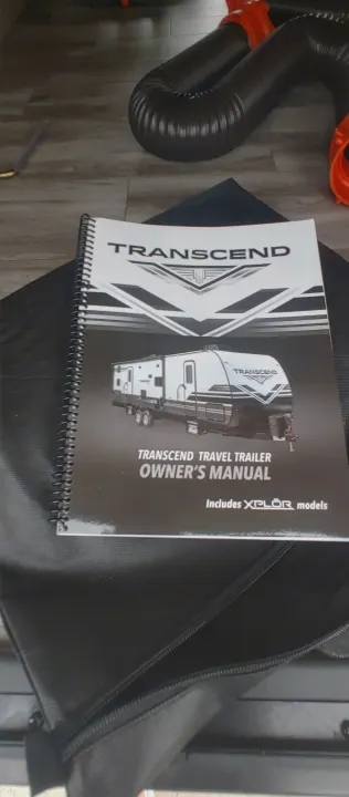 A Transcend Travel Trailer owner's manual, essential for any RV rental, is shown with a flexible wastewater hose.. Grand Design Transcend Xplor 2021