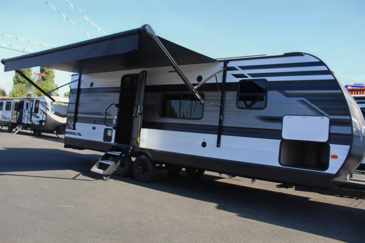This RV rental, a sleek white and black Transcend XPLOR travel trailer, features an extended awning, open door, and storage.. Grand Design Transcend Xplor 2021