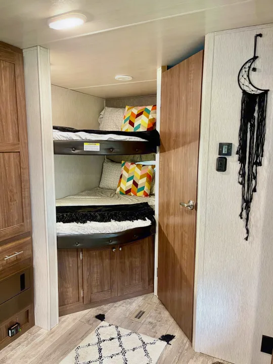 View of an RV rental's cozy bunk bed setup with colorful pillows, a wooden door, and unique moon decor inside.. Heartland Pioneer 2018