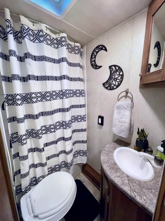 Compact RV rental bathroom with patterned shower, toilet, sink, and moon decor.. Heartland Pioneer 2018