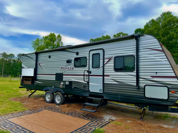 Pioneer RV rental at a sunny campsite with an extended awning and outdoor mat.. Heartland Pioneer 2018