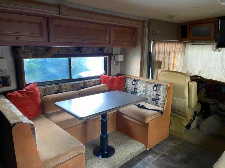 This RV rental interior features a cozy dinette with patterned seating, a spacious table, and driver's area, perfect for travel.. Itasca Sunstar 2012