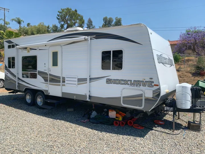 Explore the outdoors with this large white travel trailer RV rental, featuring an awning and parked on a gravel lot.. Forest River Other 2013